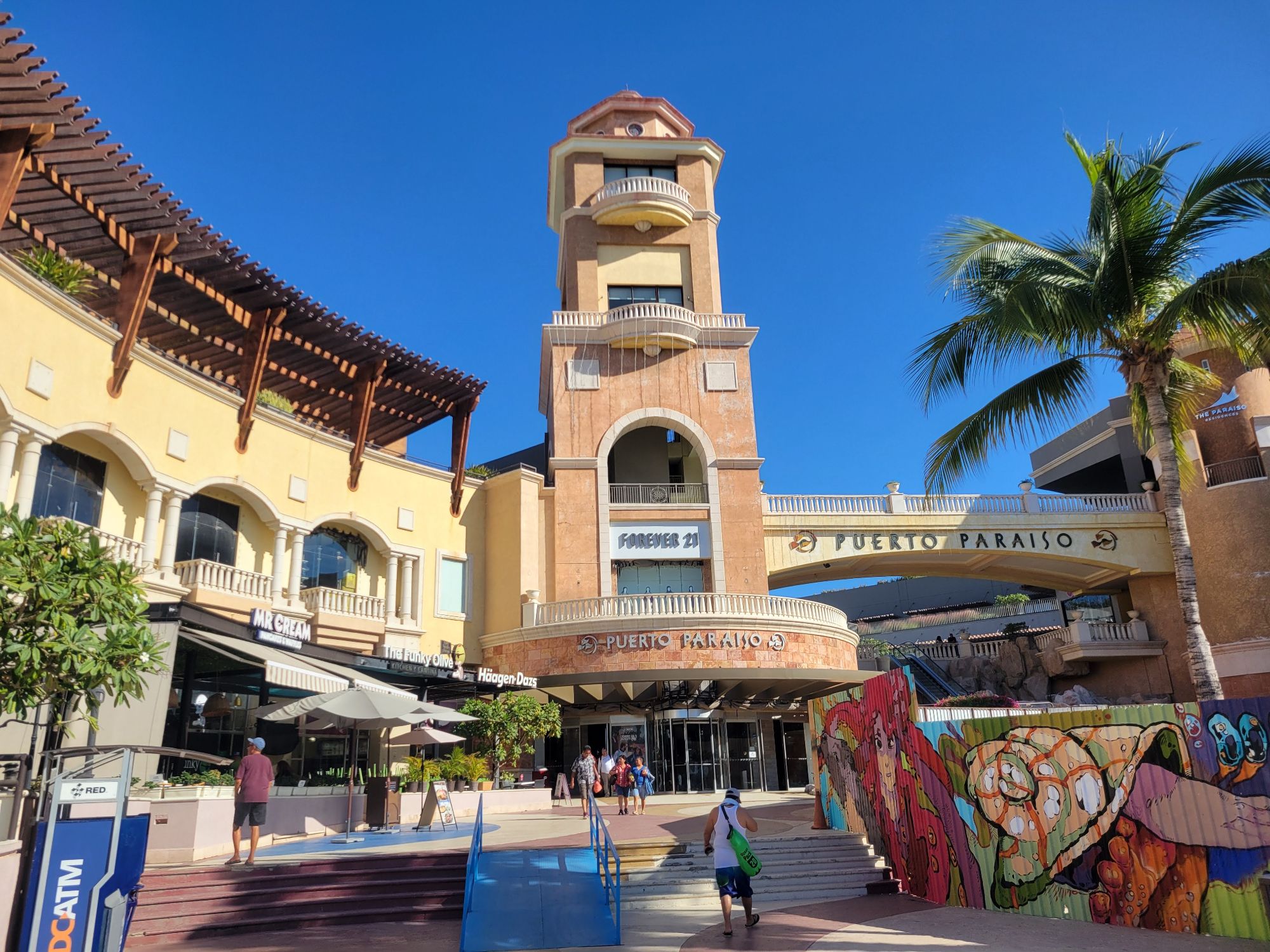 Puerto Paraiso shopping center tower with colonial architecture, palm trees, and colorful street art in Los Cabos