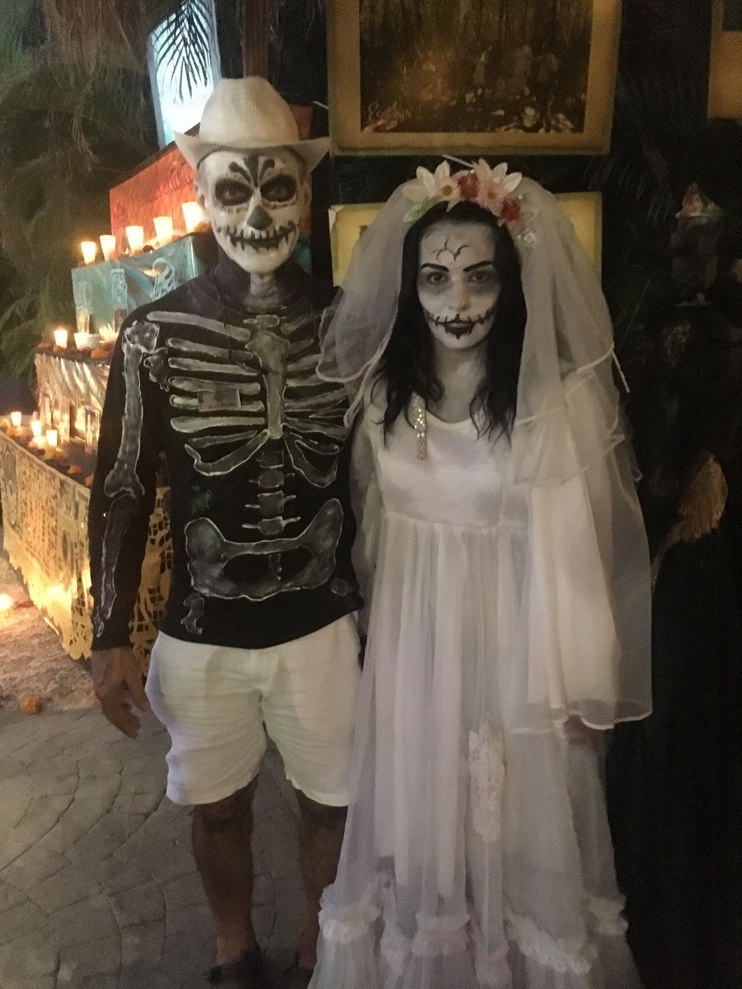 Skeleton and bride figures in skull face paint and white dress posing by candlelit grave marker for Earl C.