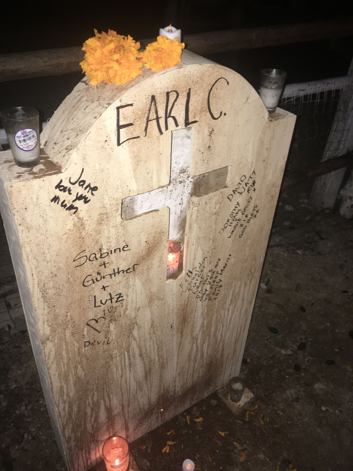 Wooden coffin-shaped grave marker with yellow flowers and candles honoring Earl C. at cemetery