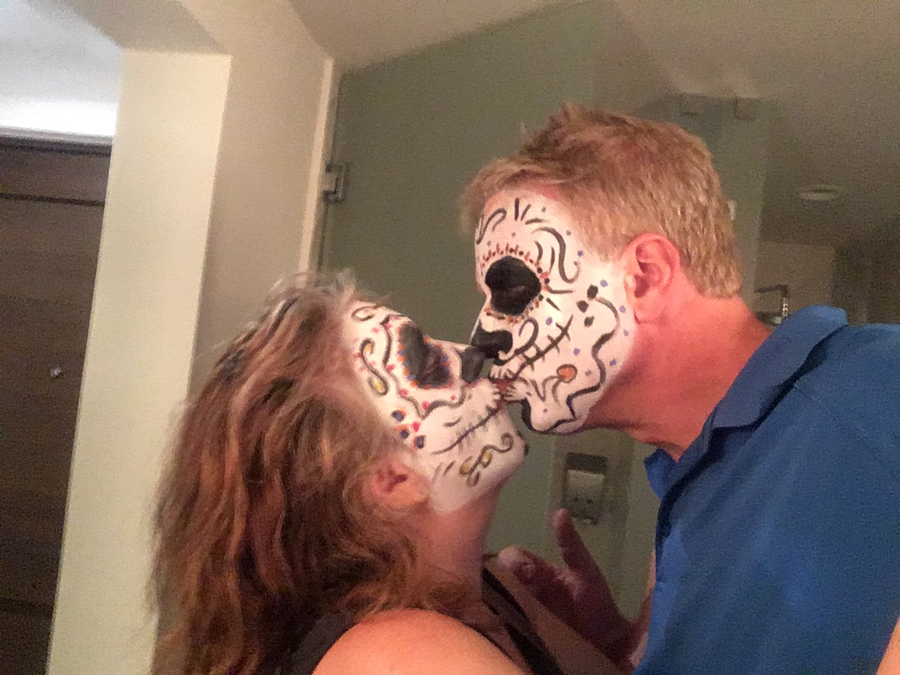 Two people with colorful skull face paint in red, black and white designs posing together indoors