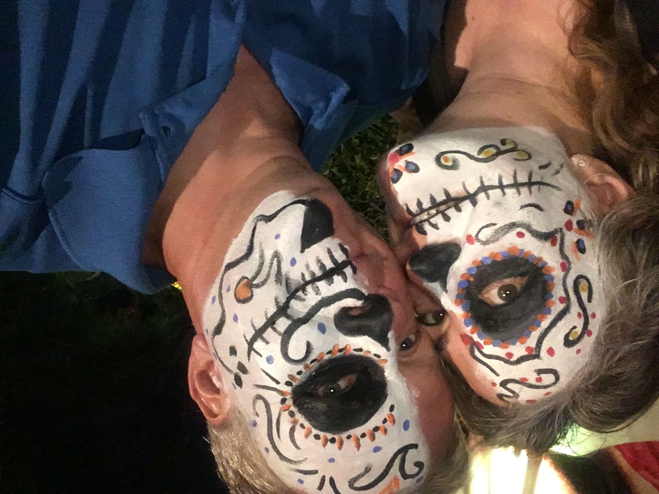 Couple wearing matching white skull face paint with decorative patterns smiling at camera outdoors