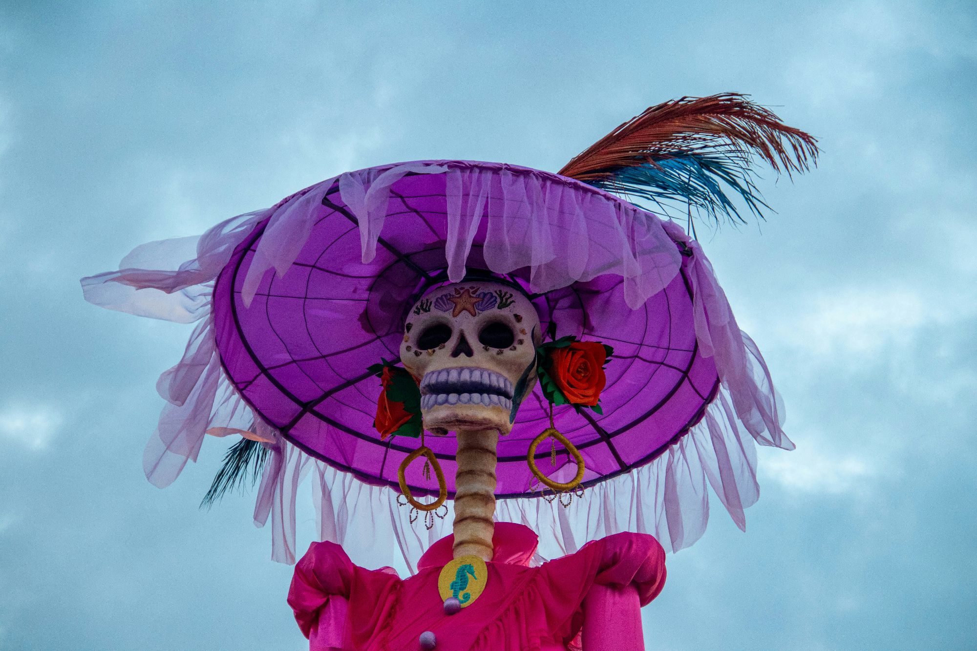 Staff member in skull face paint standing with woman at Day of the Dead altar with marigolds