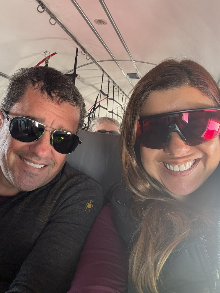 Two people smile inside a tent with visible rope rigging overhead