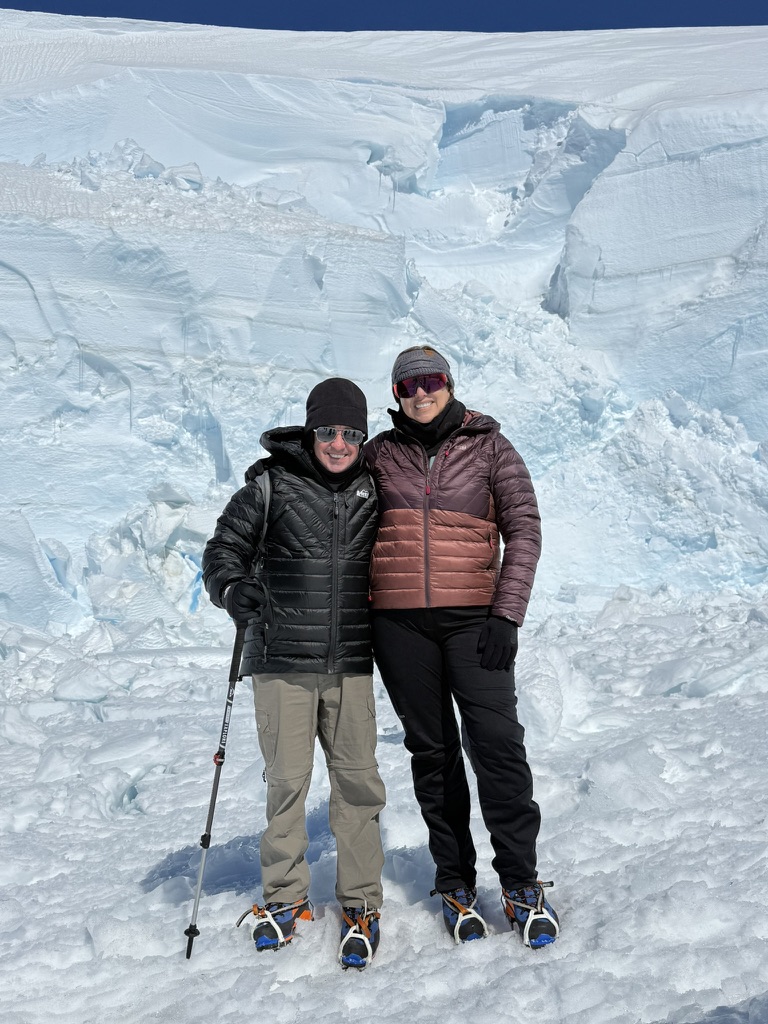 Two people in winter gear stand together in front of seracs and ice formations