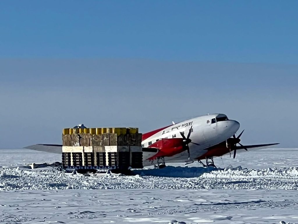 Twin Otter aircraft with cargo on Antarctic ice runway under clear blue sky