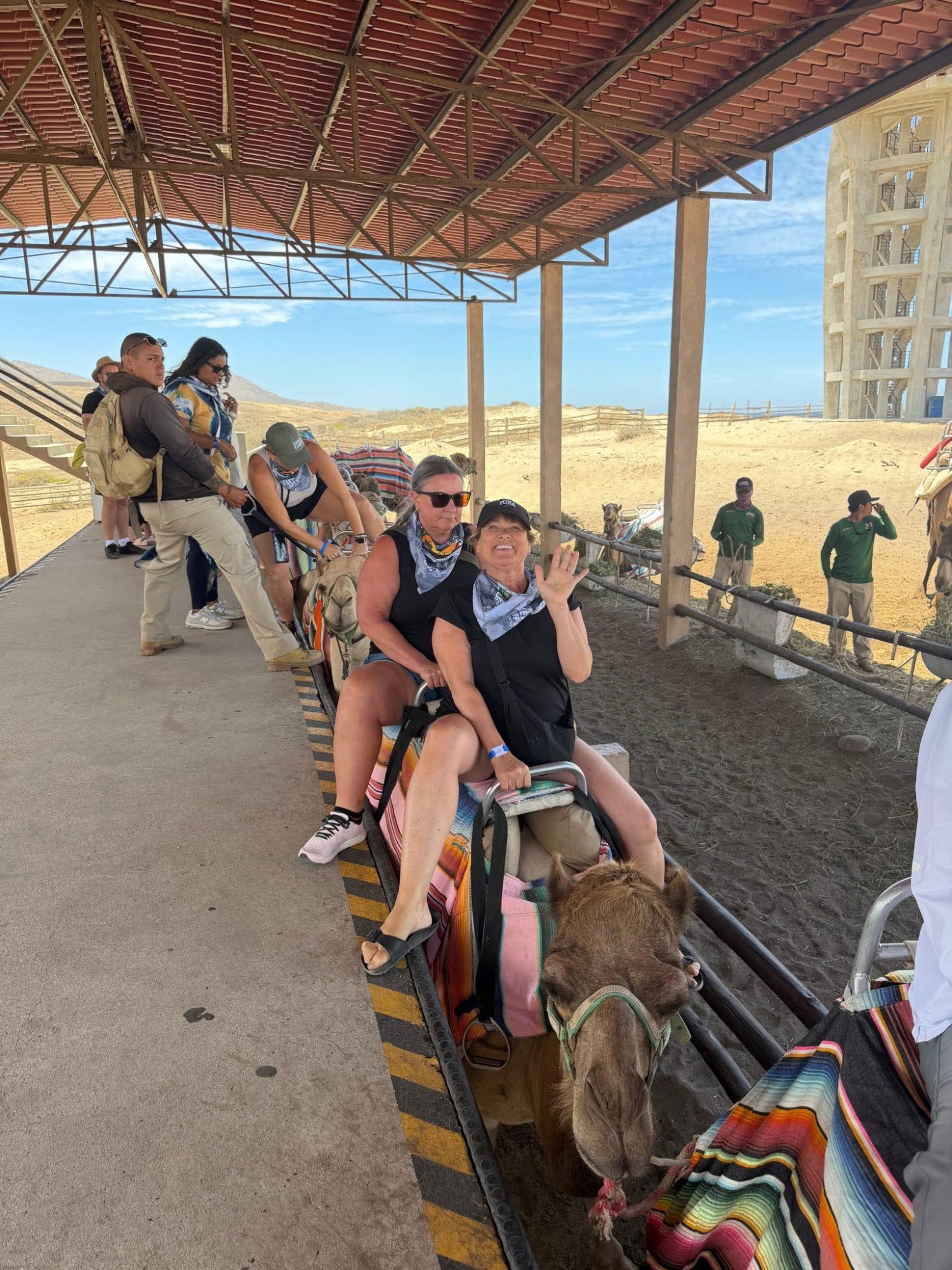 Woman on camel ride at adventure park with desert landscape and spectators in background