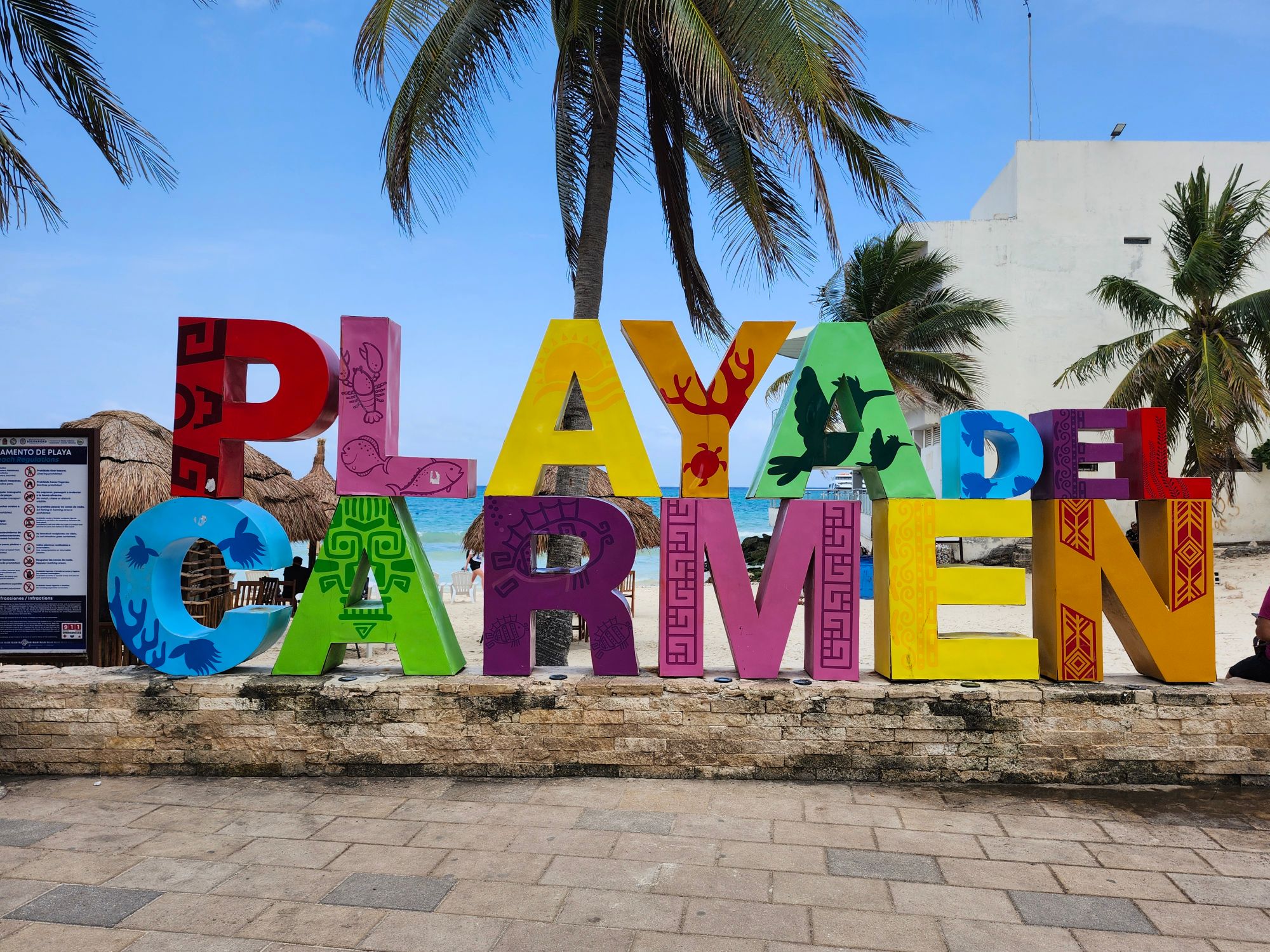 Colorful Playa del Carmen sign with beach and palm trees in background