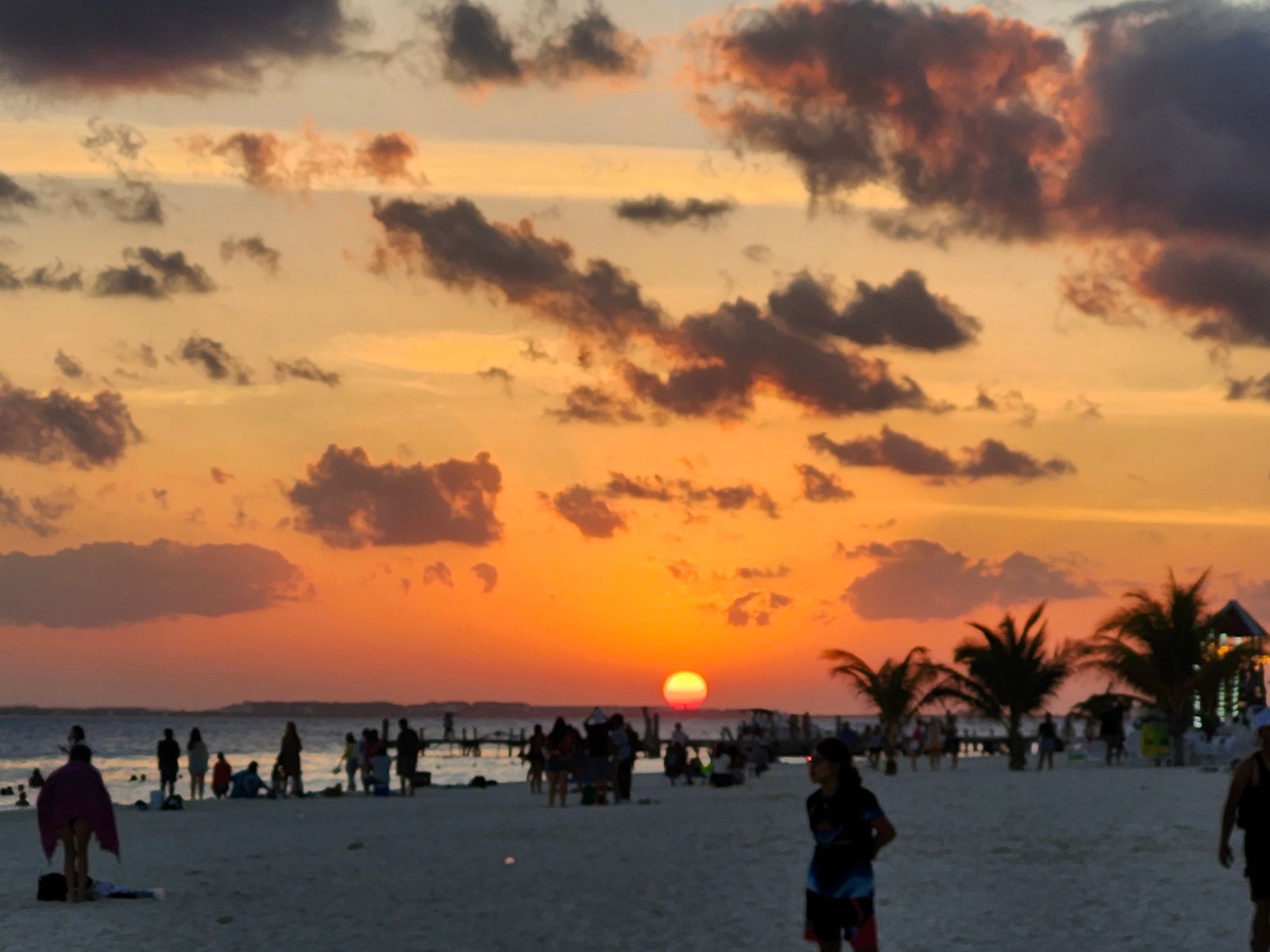Sunset over Playa del Carmen beach with crowds of people silhouetted against orange sky