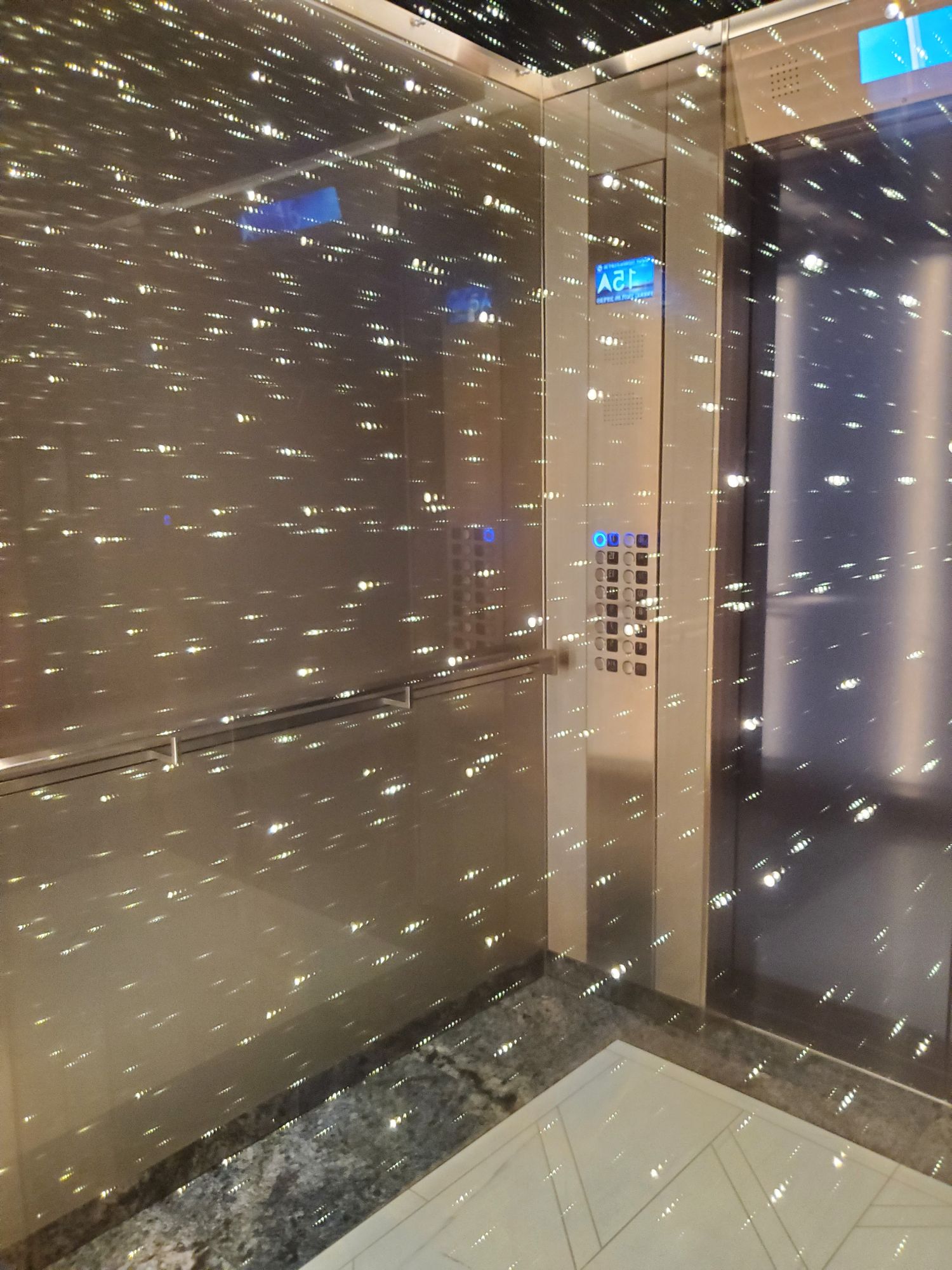 Elevator interior with perforated metal walls and blue neon signage aboard Norwegian Luna