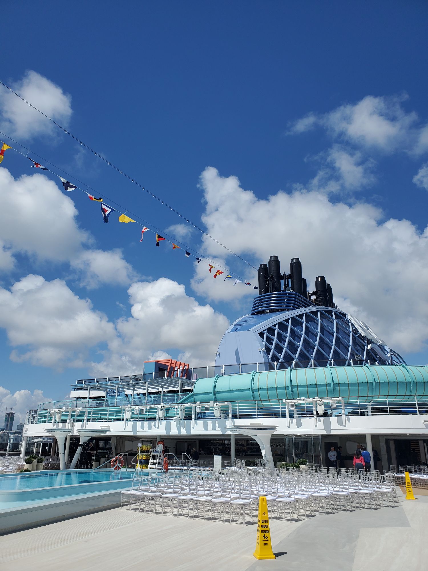Deck view of Norwegian Luna's pool area with white chairs and colorful signal flags strung overhead