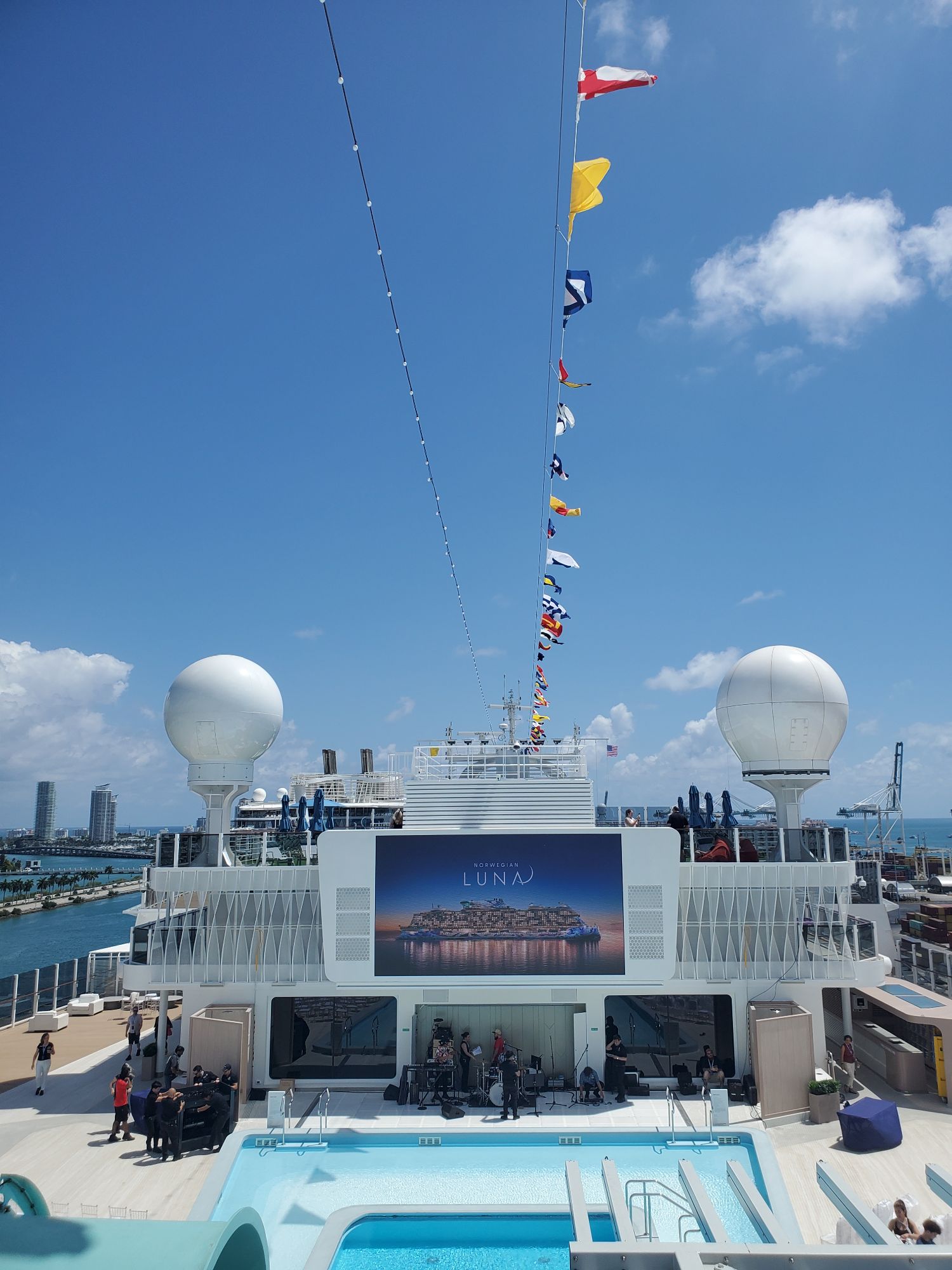 Norwegian Luna's deck with international maritime flags on mast, pool area, and ocean backdrop