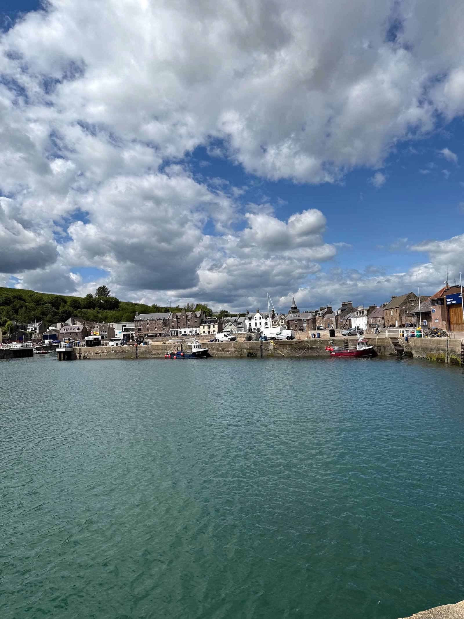 Turquoise harbor with moored fishing boats and stone buildings nestled along the waterfront under cloudy sky