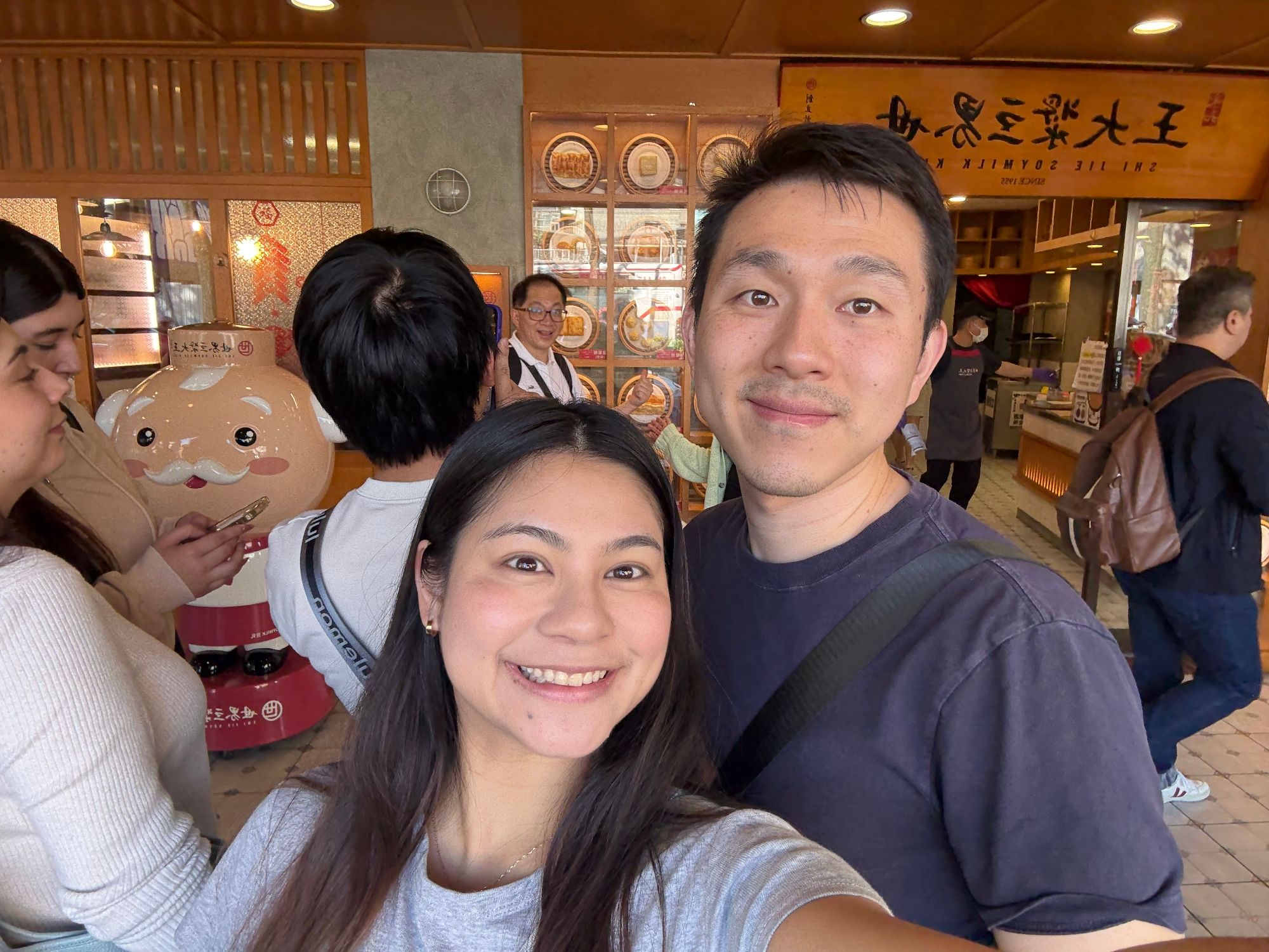 Kelly and a man smile together at a casual dining establishment with Japanese signage and decorative elements in the background