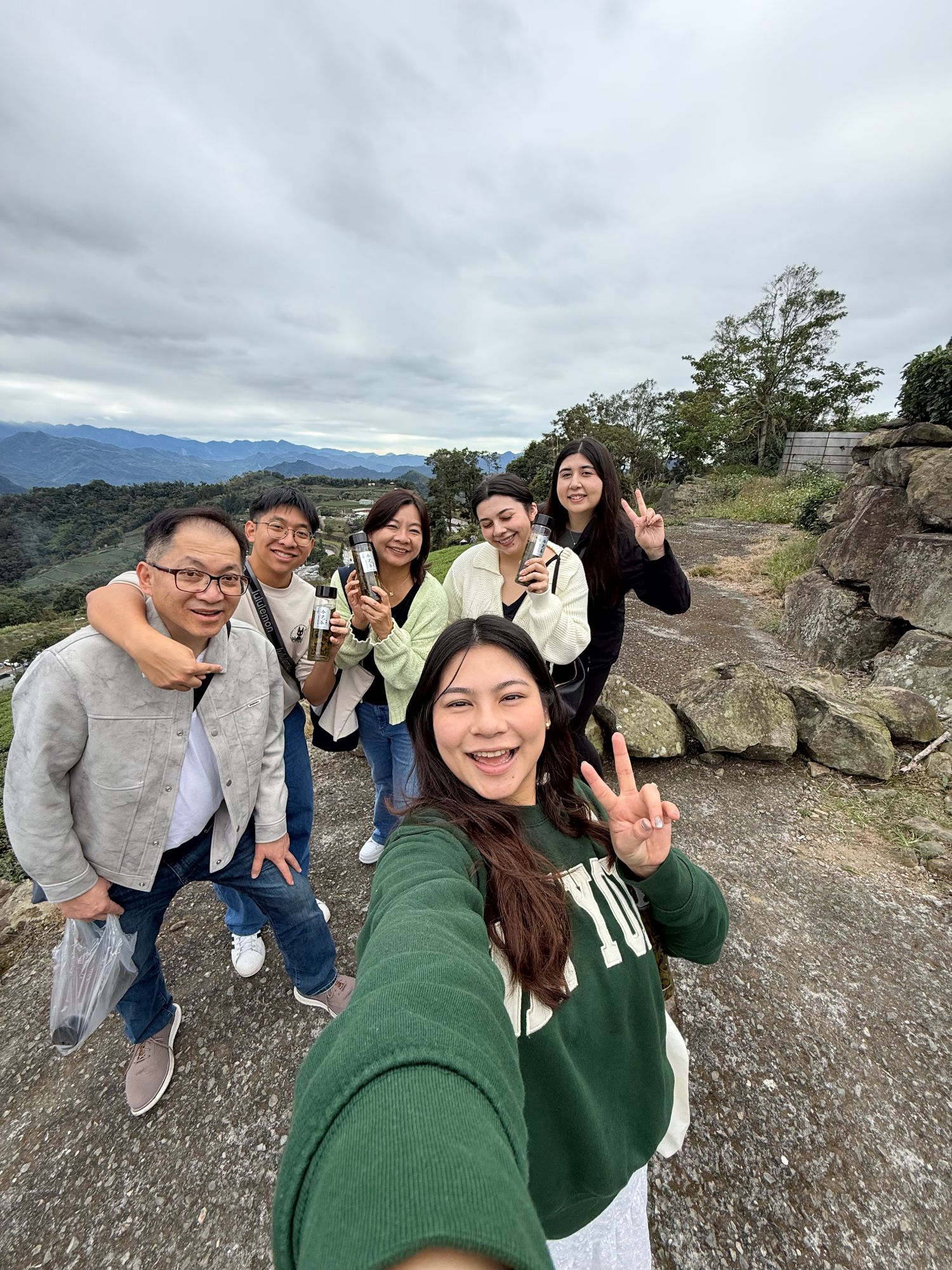 A group of six people smile at the camera while standing outdoors with mountains and forested landscape in the background