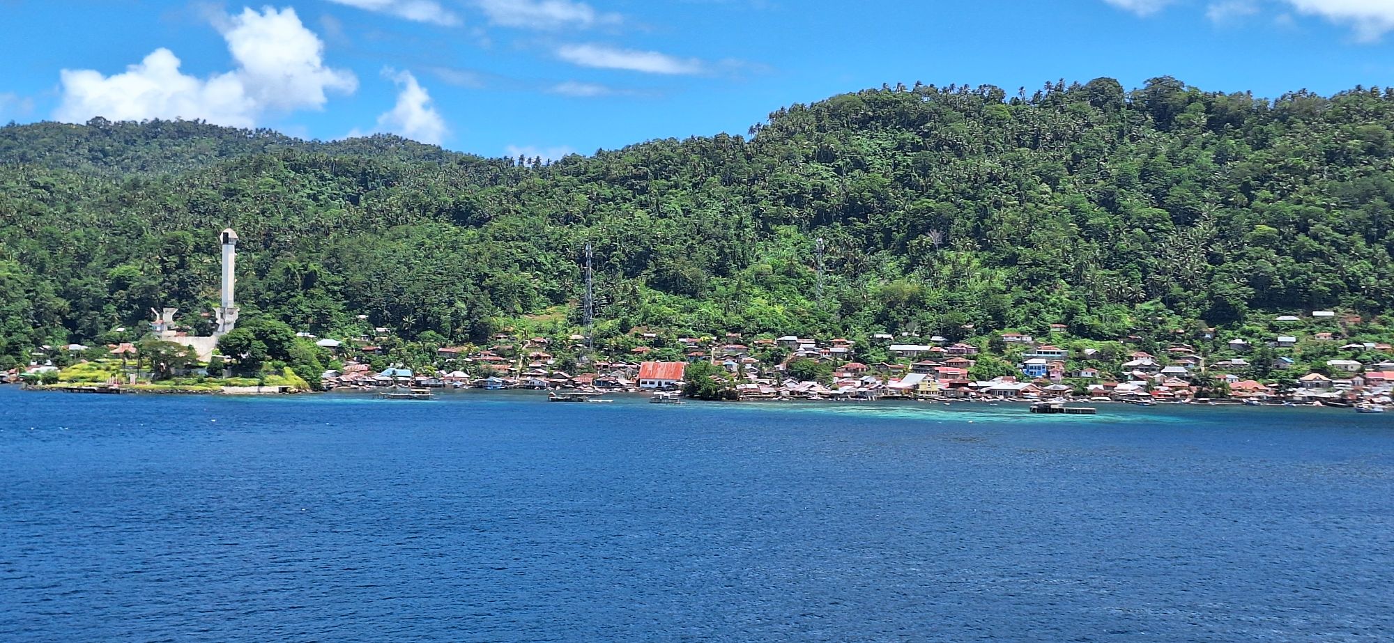 Coastal settlement with traditional houses nestled against densely forested mountainside in Bitung region