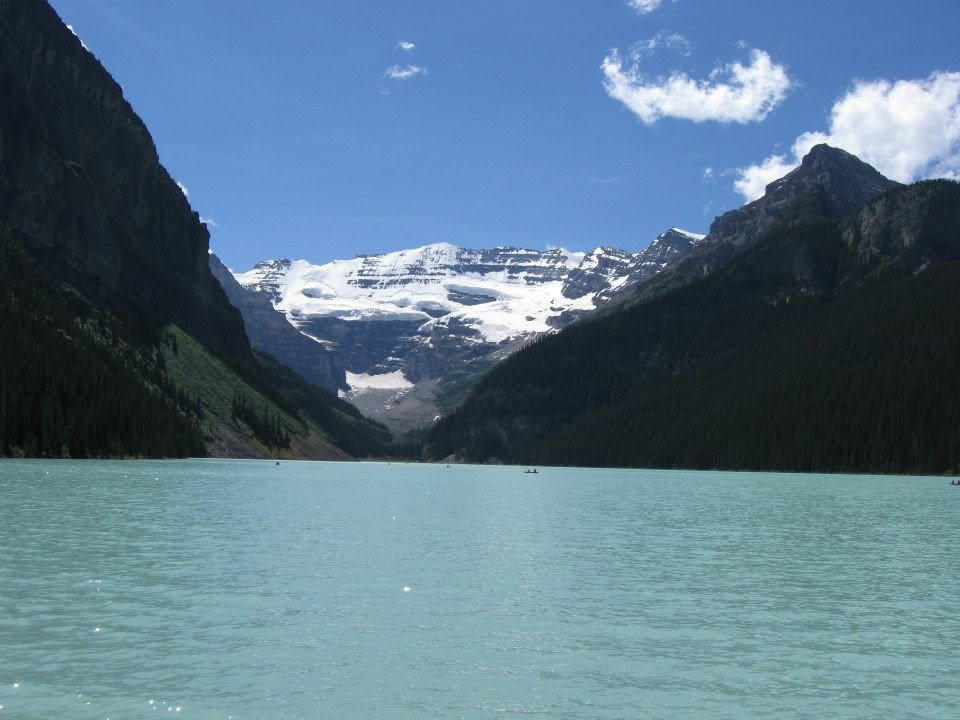 Turquoise glacial lake surrounded by steep mountain cliffs and forested slopes