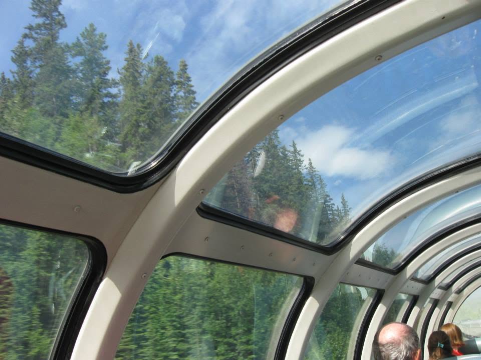 Dining table set with white tablecloth and place settings inside a train car with window views