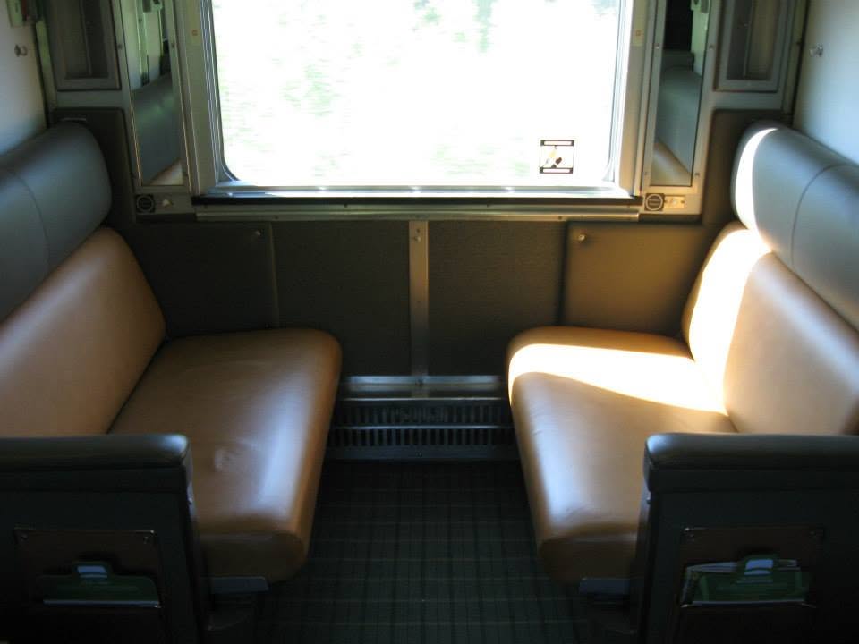 Two people toasting with drinks inside a train dining car with forest scenery outside