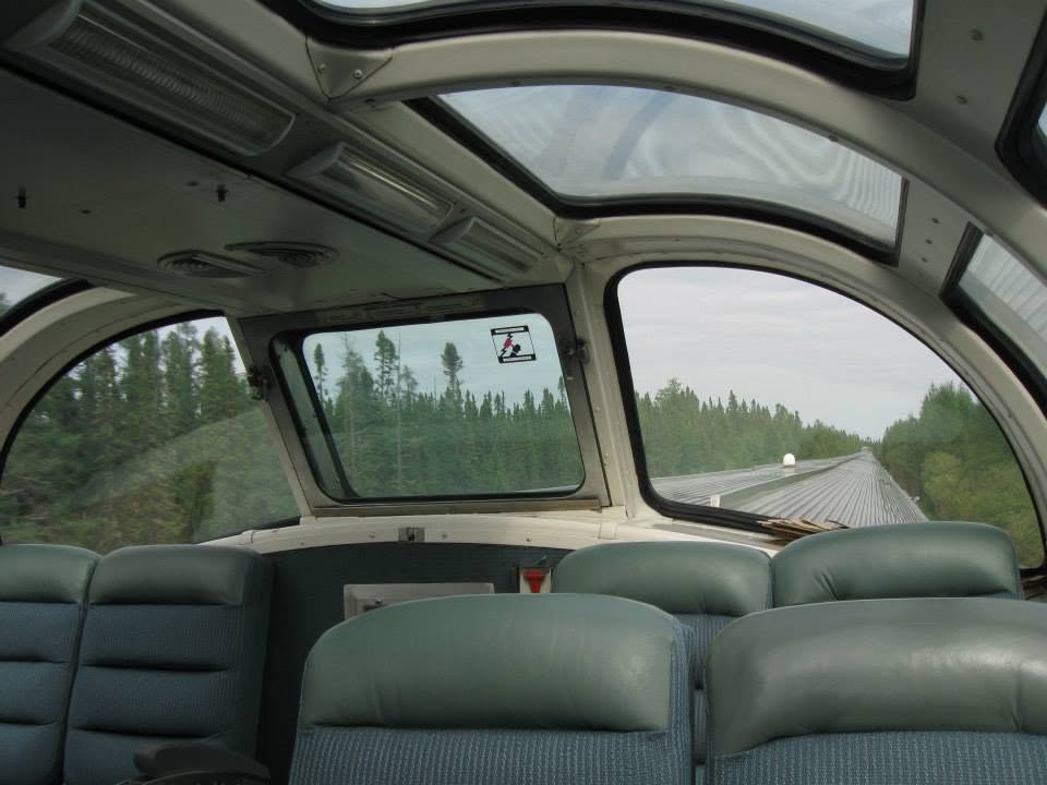 Interior view of a train car showing seats and forward-facing windows with landscape