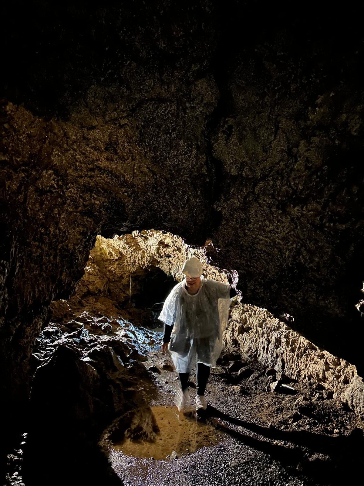 Person in white shirt exploring inside a cave with golden-brown rock walls and natural light opening