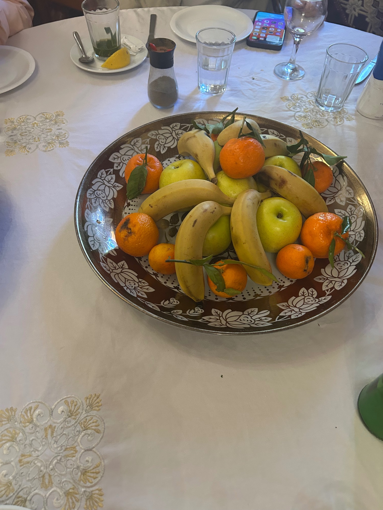Decorative plate of fresh fruit including bananas, apples, and oranges on a patterned metal platter