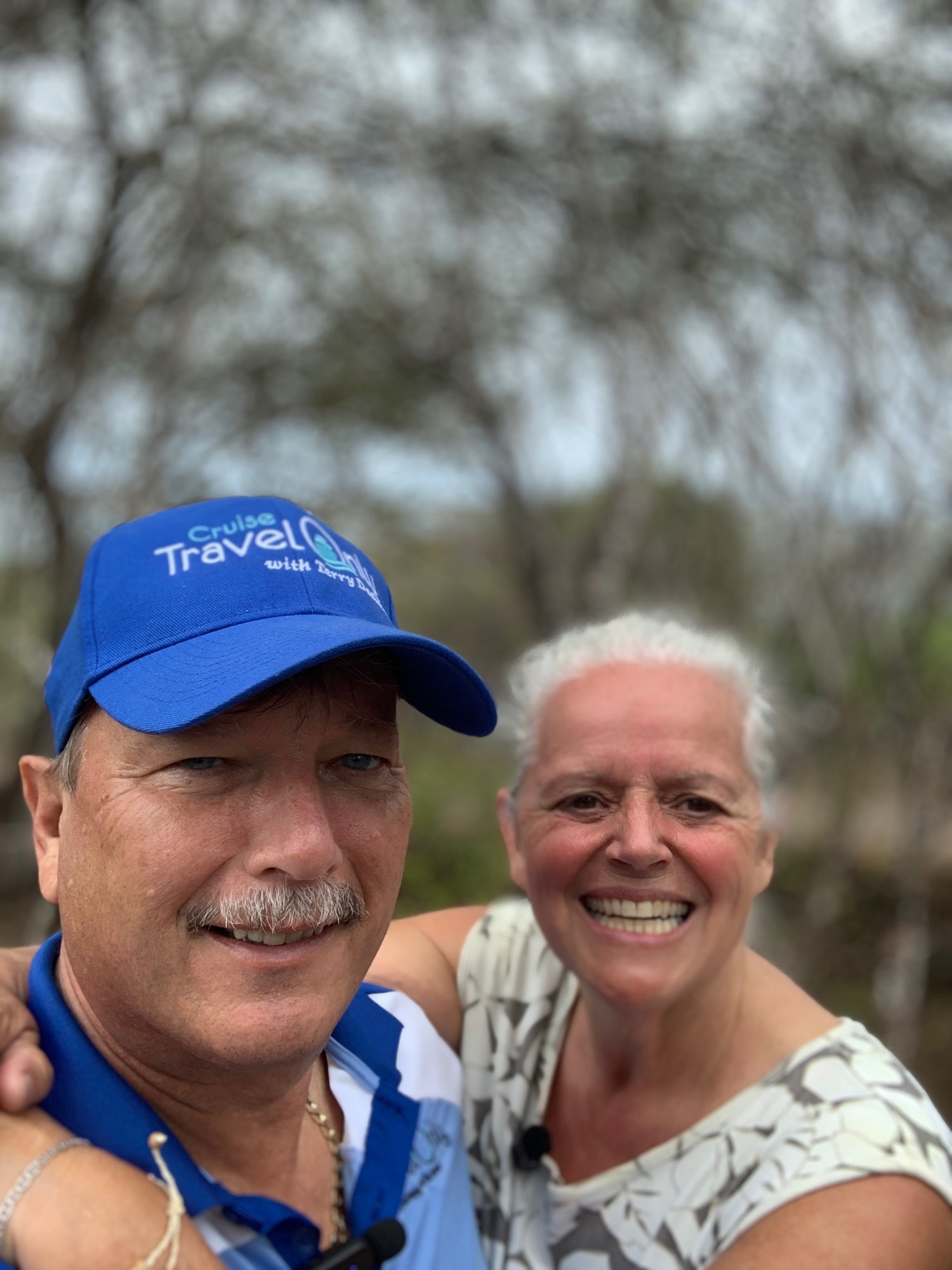 Two travelers smiling at camera with white-haired woman on left wearing blue jacket