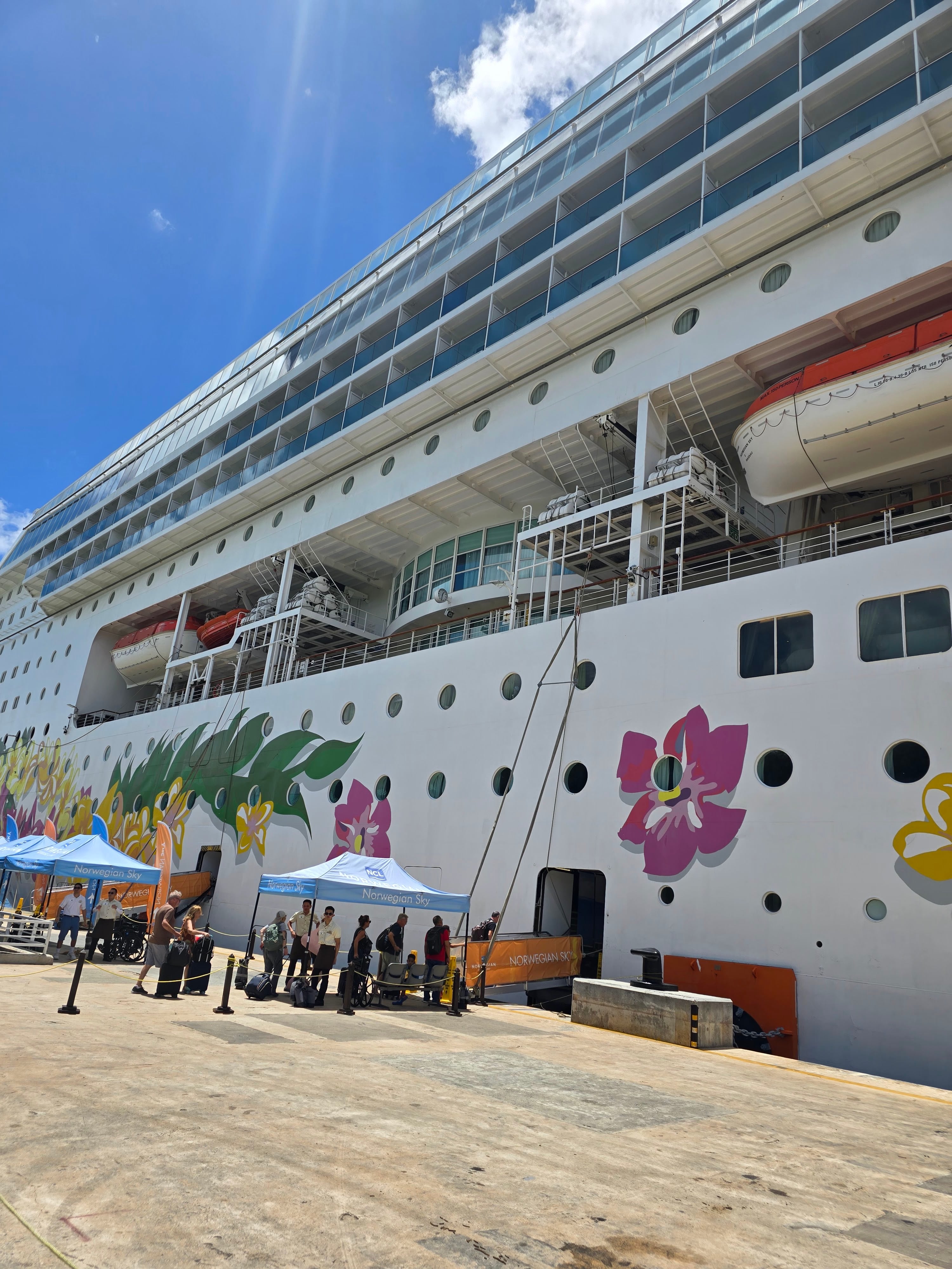 Norwegian Sky cruise ship moored at dock with passengers boarding via gangway under blue sky