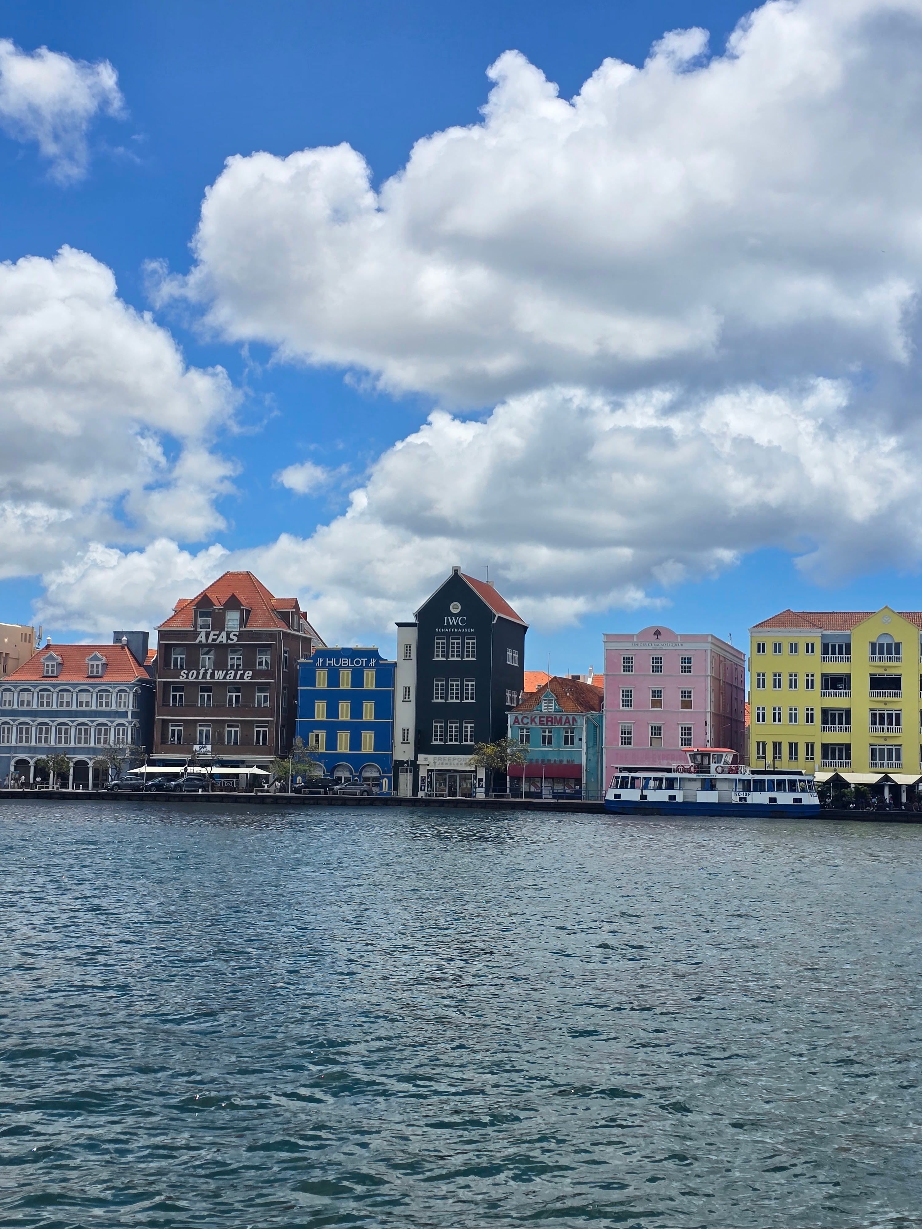 Waterfront row of pastel-colored colonial buildings reflected in calm Caribbean waters