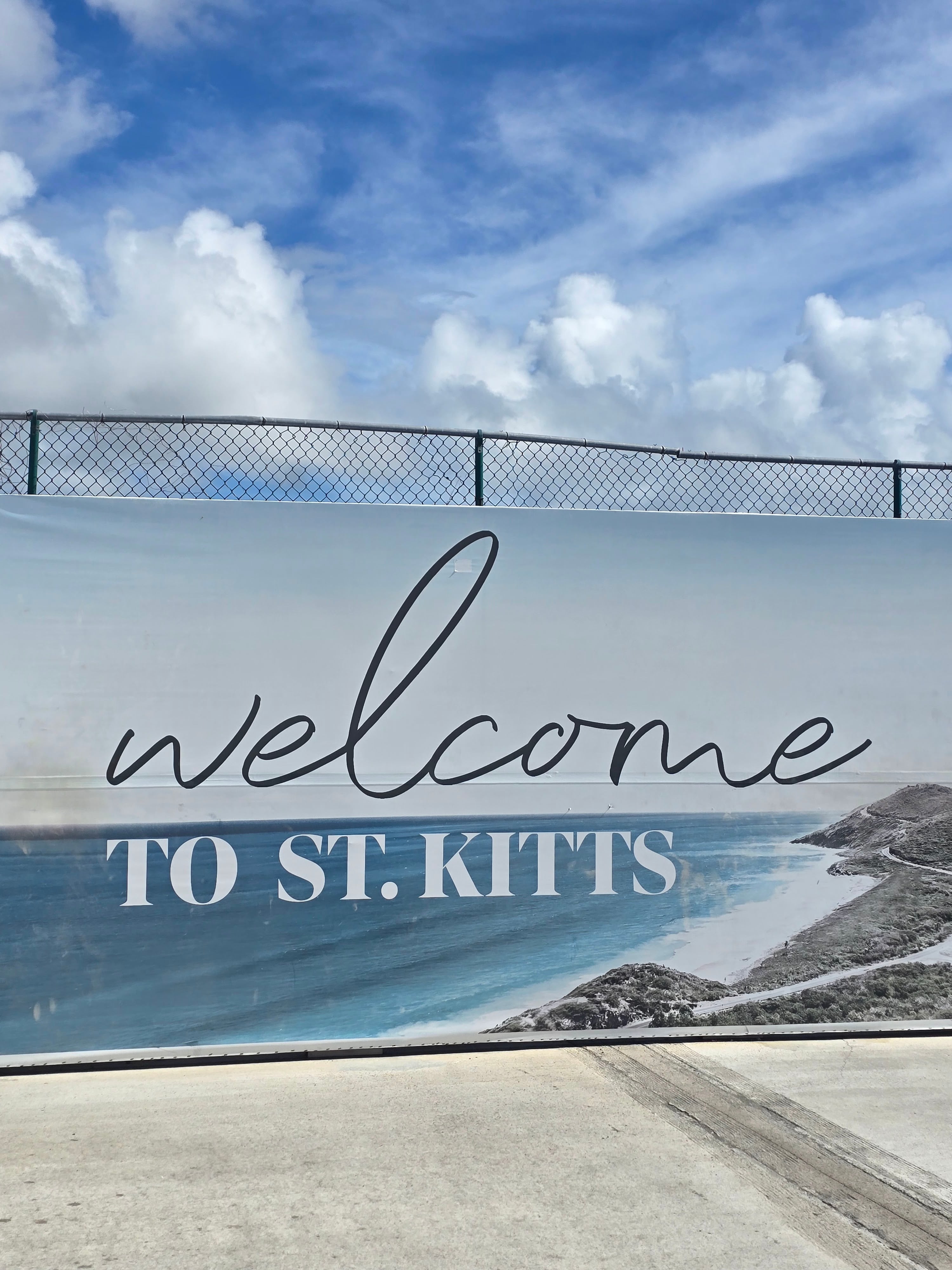 Welcome sign to St. Kitts with turquoise ocean and beach visible in background
