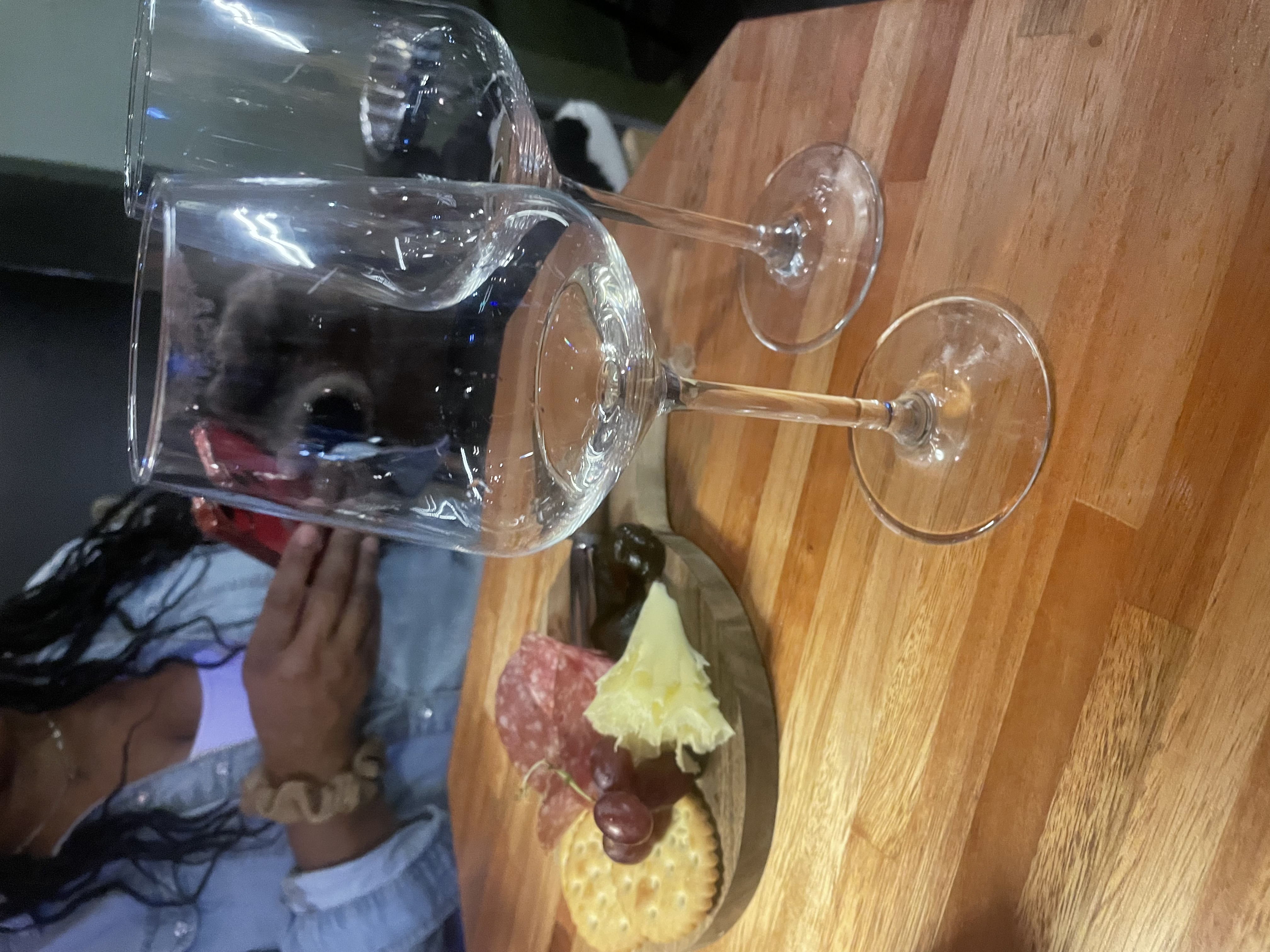 Two wine glasses on a wooden table with charcuterie board, woman's hand reaching toward them