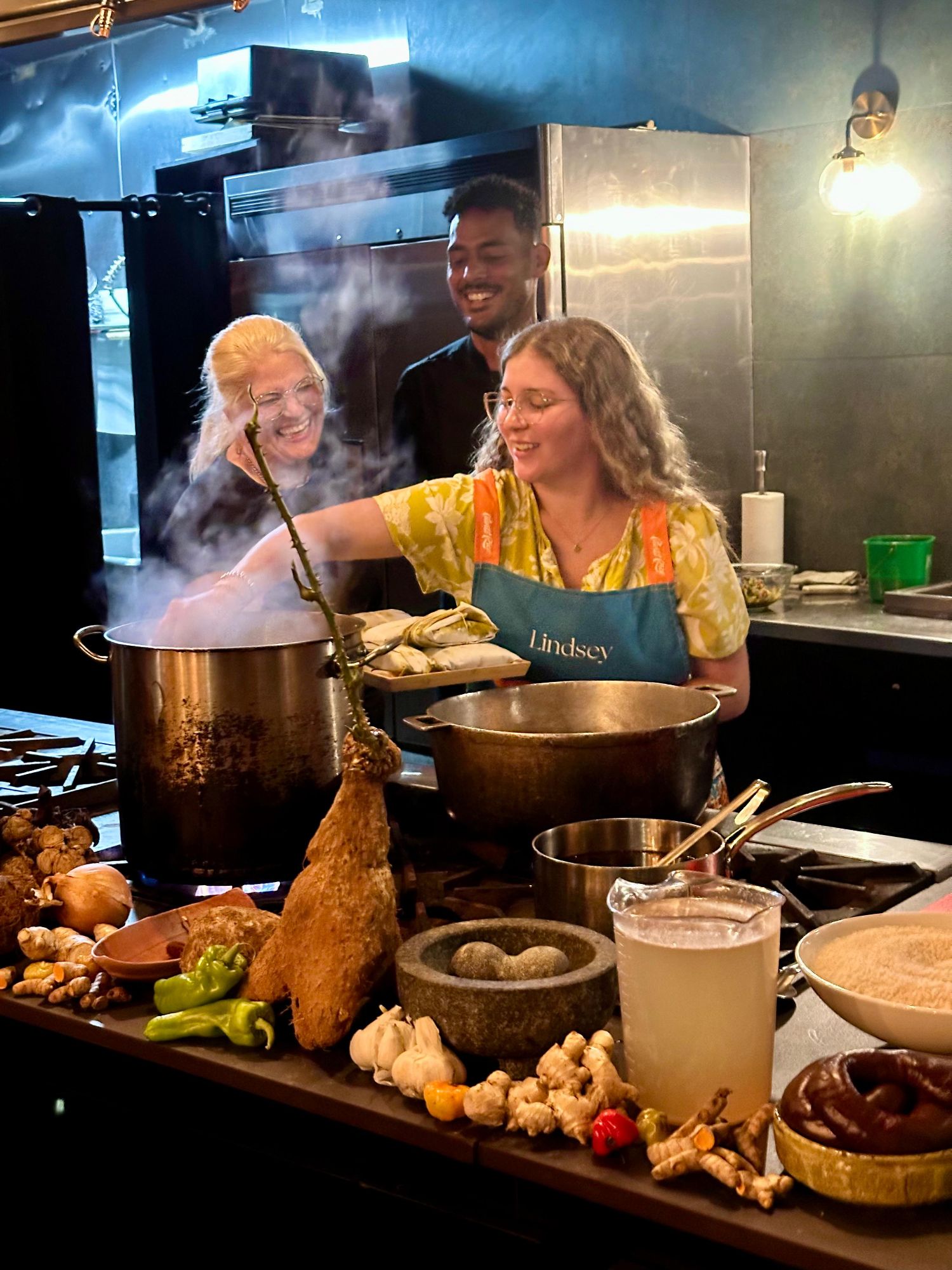Woman in yellow apron stirring large pots during a cooking demonstration in a modern kitchen
