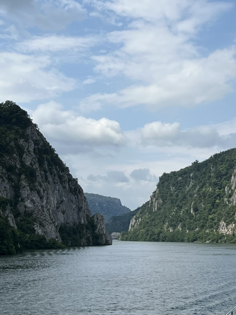 Steep limestone canyon walls frame a calm stretch of the Danube River with forested slopes under cloudy skies