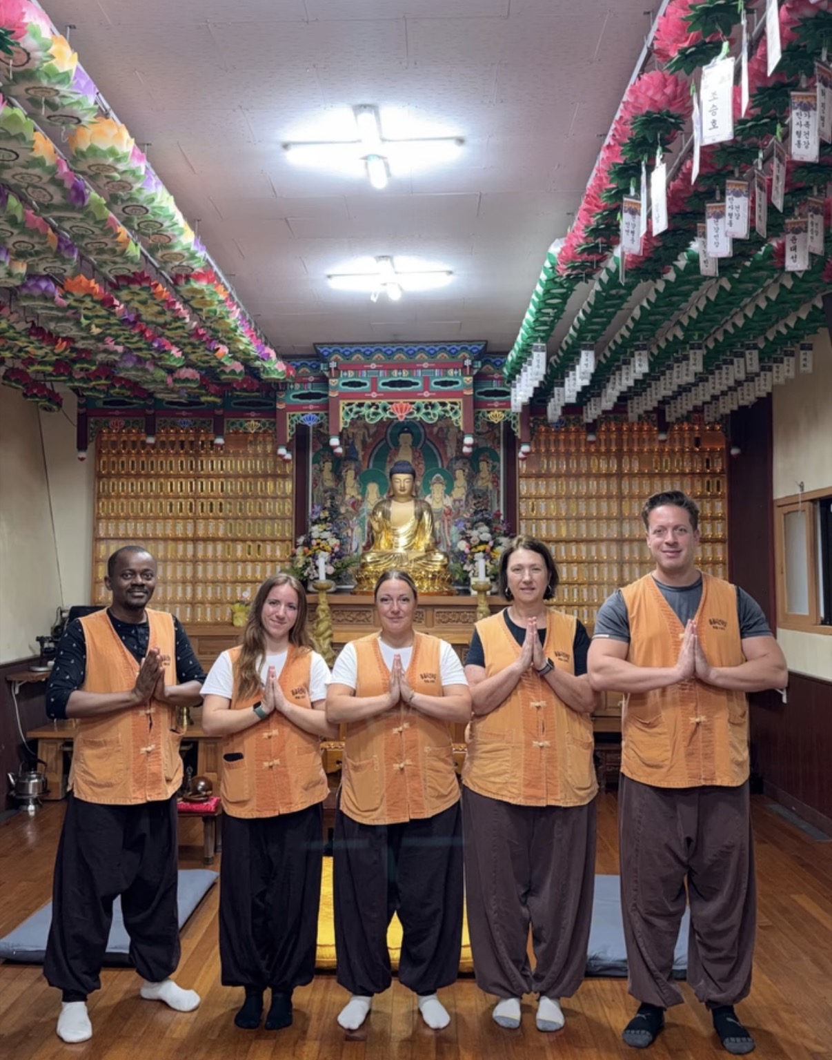 Five people in yellow and brown volunteer vests with hands pressed together in a Buddhist temple