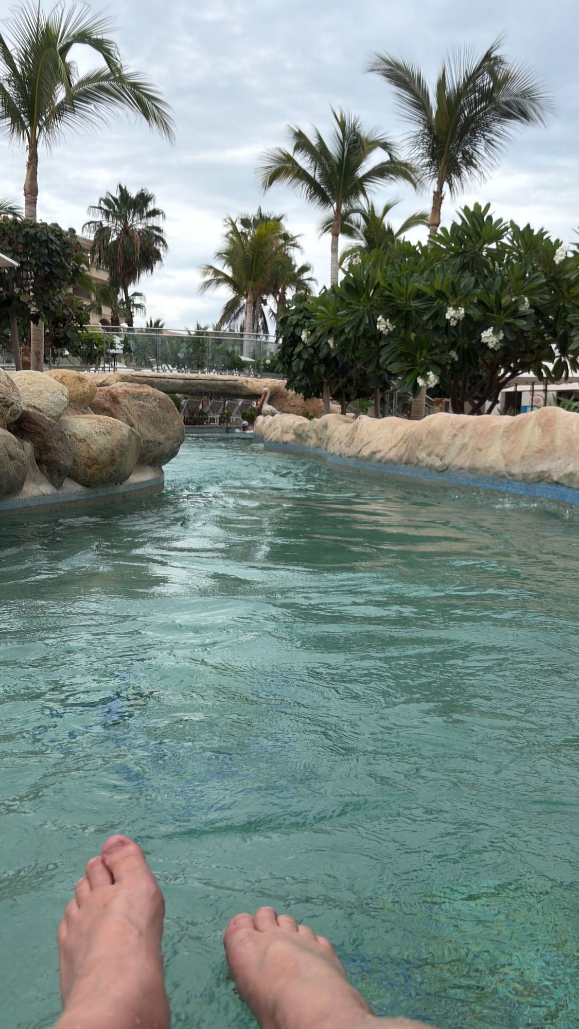Tropical lagoon with clear turquoise water, large boulders, palm trees, and a bridge crossing the shallow water