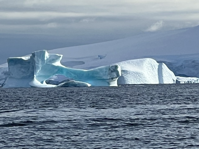 A large blue and white iceberg floats in Antarctic waters with mountains visible in the background