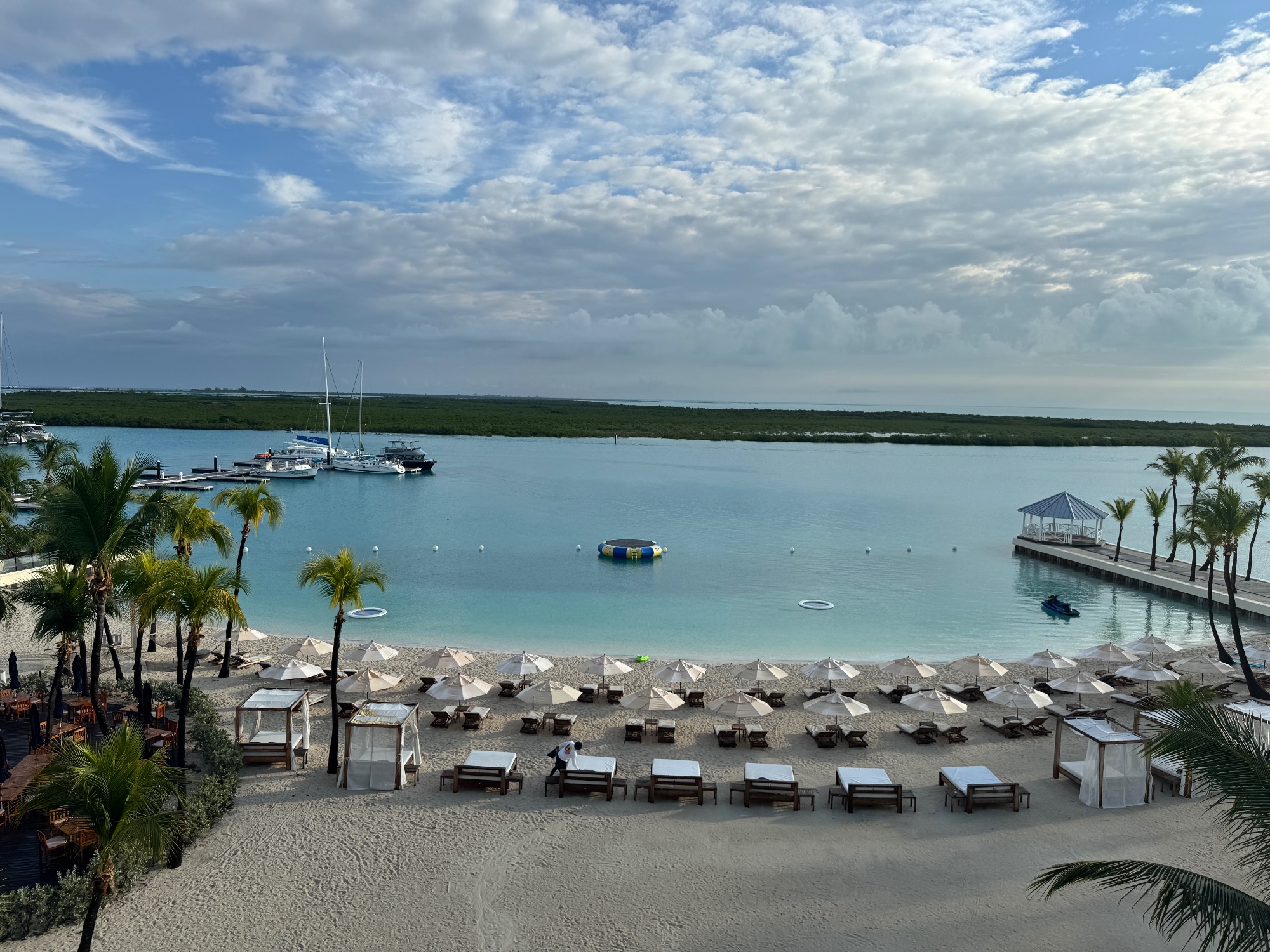 Aerial view of beach with white umbrellas, lounge chairs, palm trees, boats, and turquoise water in Turks and Caicos