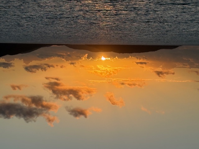 Sunset over calm Caribbean waters with silhouetted islands on the horizon and golden-orange sky