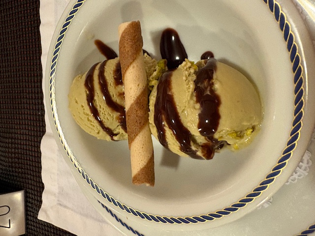Vanilla ice cream with chocolate sauce and a wafer cookie on a plate with nautical rope-pattern rim