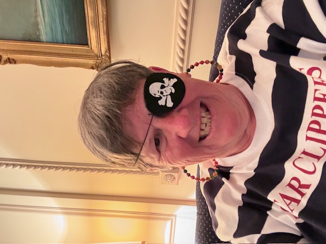 Person wearing a pirate eye patch and striped shirt smiling at the camera indoors