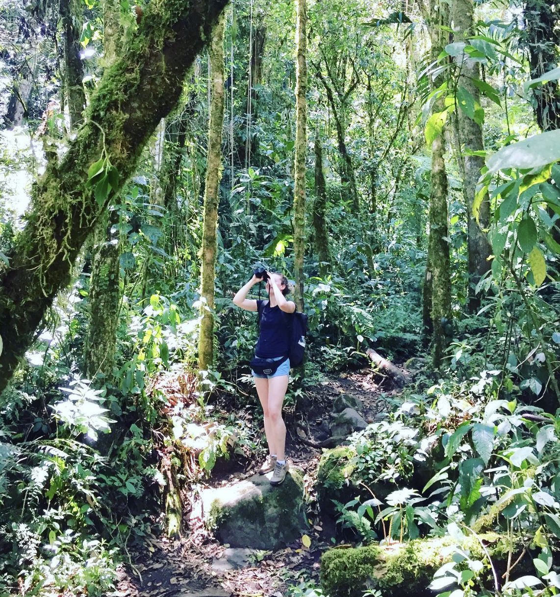 Autumn Fiske jogging through a lush Panama cloud forest on a narrow trail surrounded by moss-covered trees and dense tropical vegetation