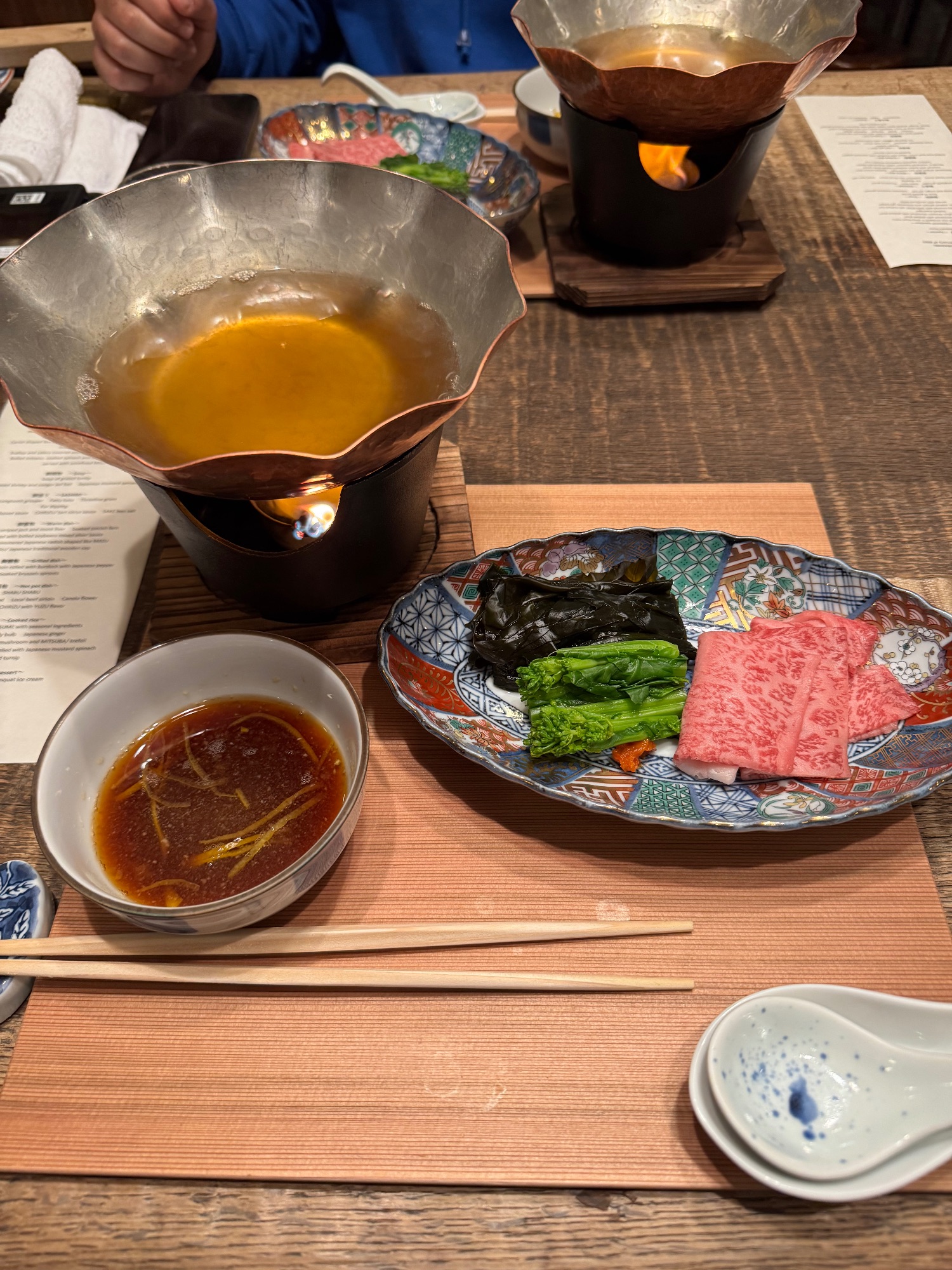 Duncan Greenfield-Turk examines sliced wagyu beef and vegetables beside bowls of broth at a Japanese dining table