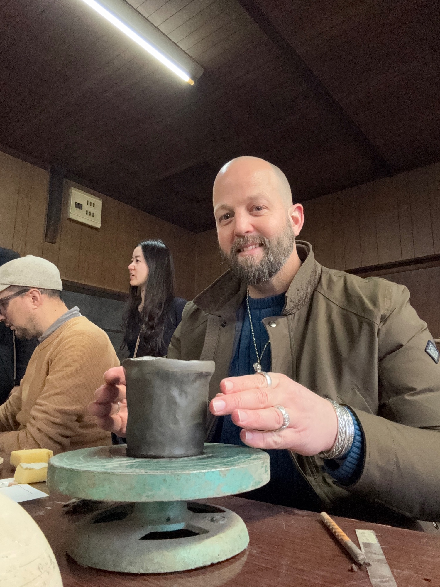 Duncan Greenfield-Turk holds a ceramic cup at a pottery workshop in Japan with other participants visible in the background