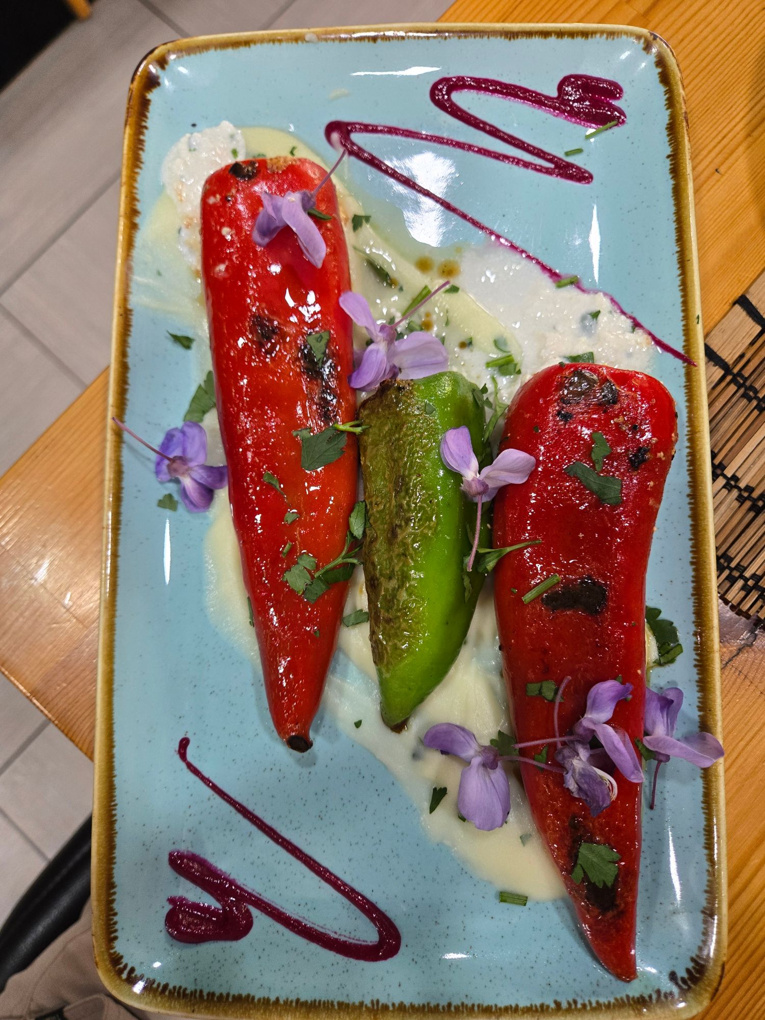 Plated dish with roasted red peppers, green pepper, white cheese, and purple flowers on a light blue ceramic plate