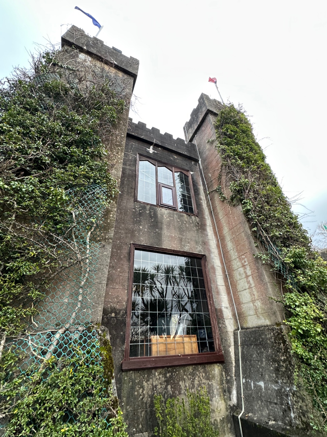 Tall stone tower with crenellations and ivy-covered walls, flying a flag by the waterside