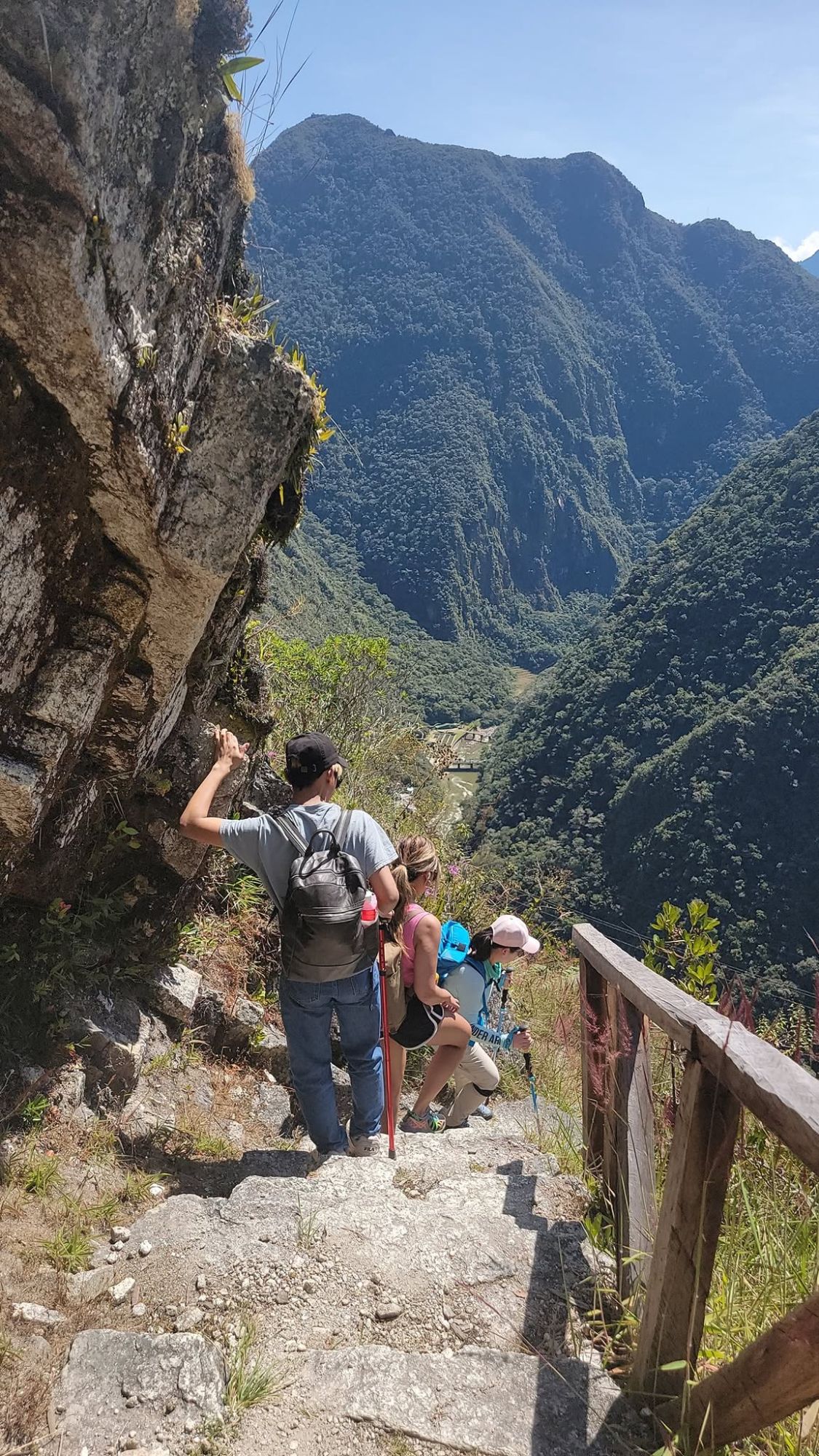 Hikers navigating a narrow stone pathway carved into a steep mountainside with dramatic valley views below