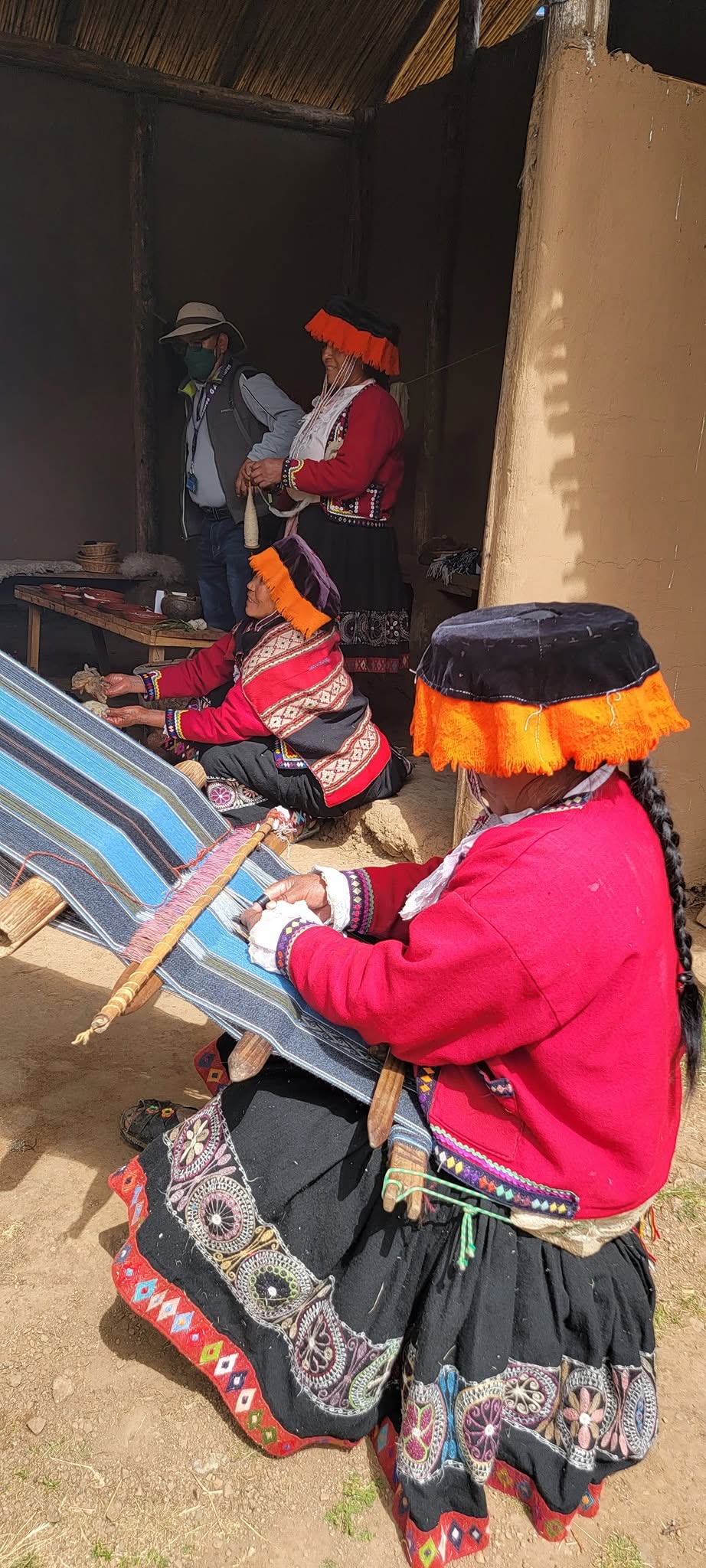 Indigenous Peruvian women in traditional red clothing and woven textiles demonstrating traditional weaving techniques