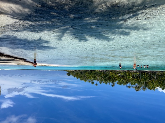 Row of green plastic chairs on white sand beach facing turquoise lagoon and palm trees
