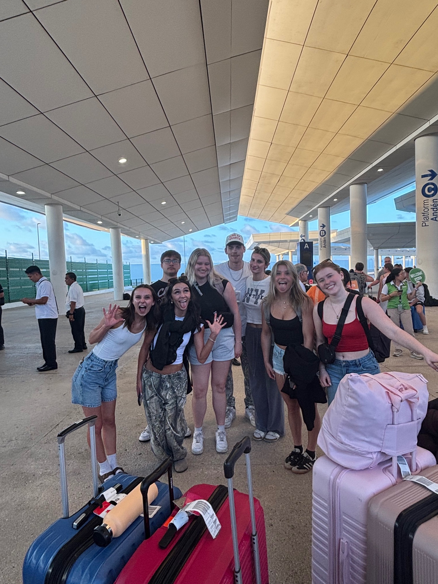 Group of young adults posing happily at an airport terminal with colorful luggage in foreground