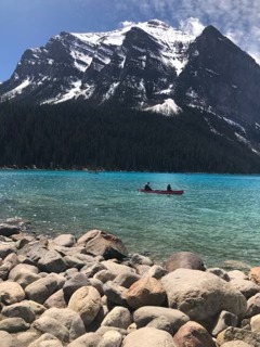 Turquoise alpine lake surrounded by rocky shores and evergreen forest with snow-capped peaks in the background