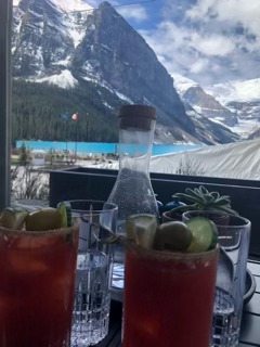 Cocktails with red liquid and lime garnish on a table overlooking a snow-capped mountain landscape